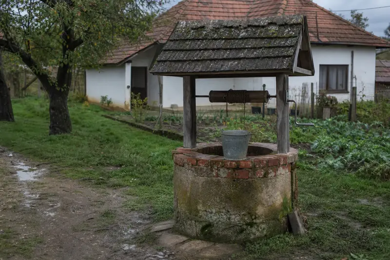 Klasická kopaná studňa s drevenou strieškou v záhrade rodinného domu.