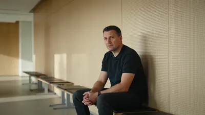 Človek sedí v čakárni úradu práce s dokumentmi v ruke, v pozadí informačná tabuľa
