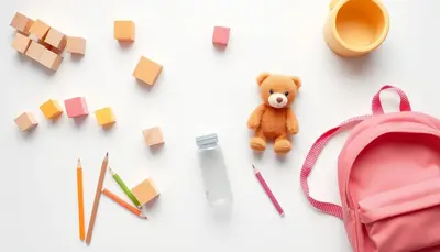 Detské veci na bielom pozadí – kocky, plyšák, pastelky a batôžtek