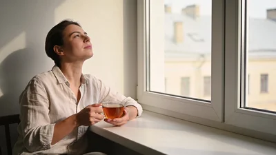 Človek pri okne premýšľa nad správou v telefóne pri rannom svetle