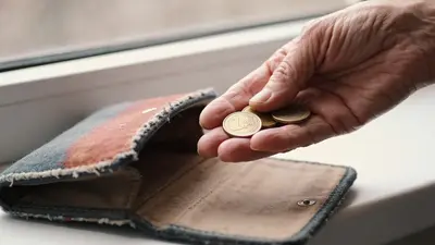 Ruka drží pár drobných mincí nad prázdnym vreckom