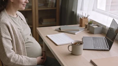 Tehotná žena sedí pri pracovnom stole s diárom a hrnčekom teplého čaju