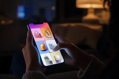 Ruka drží smartfón s nakupovacou aplikáciou v tmavej miestnosti