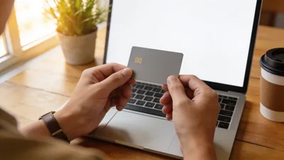 Podnikateľ drží platobnú kartu nad klávesnicou notebooku pri pracovnom stole